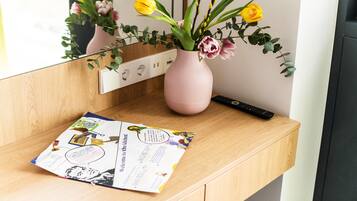 Un bureau en bois sur lequel se trouve un vase rose contenant des fleurs jaunes et une télécommande.