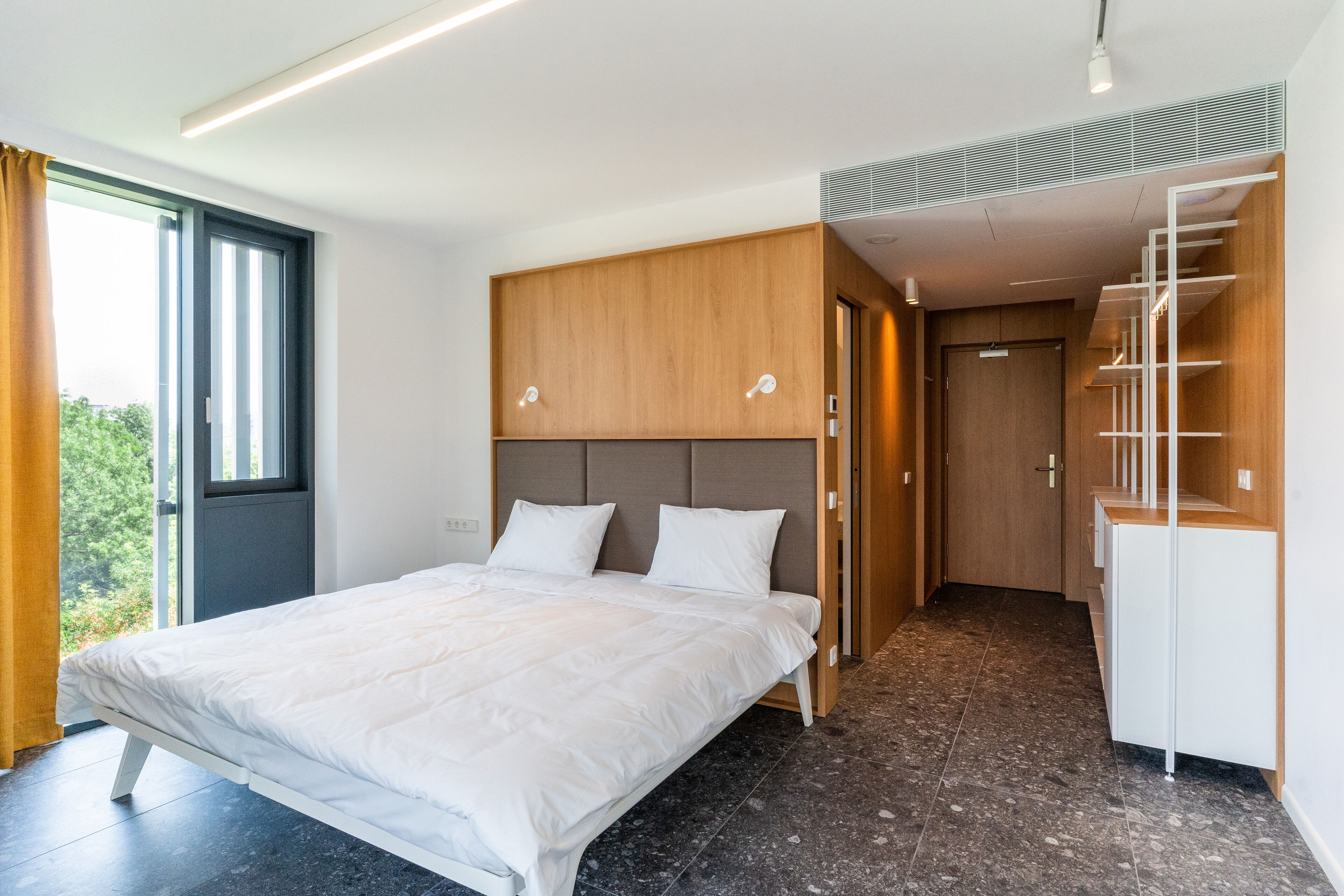 A modern bedroom with a large bed, built-in wardrobe, and a view of the outdoors.
