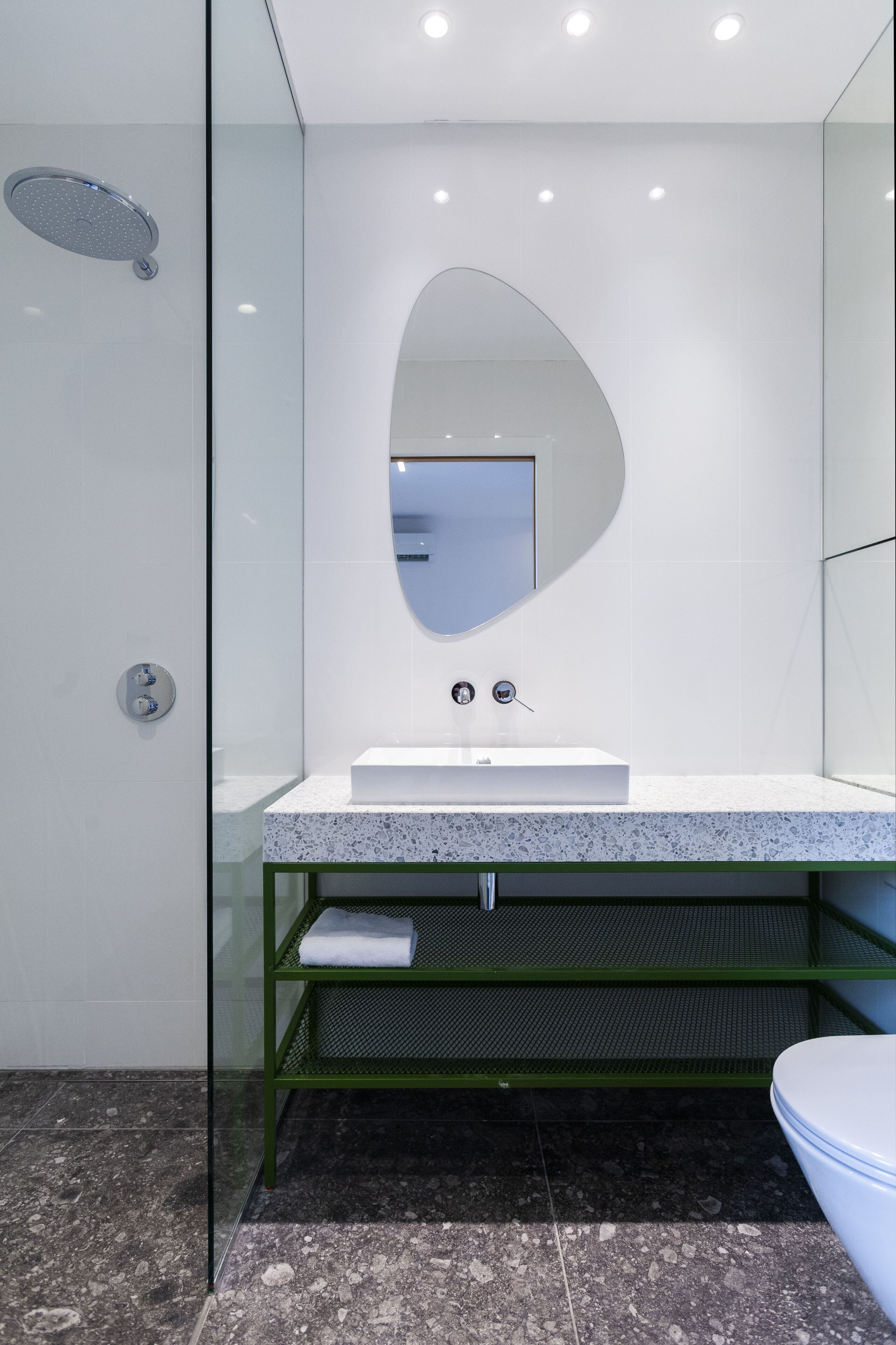 Un baño moderno con ducha de vidrio, un lavamanos blanco y un estante verde, y un inodoro.