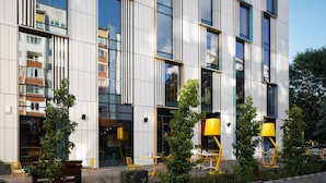 Un edificio moderno con amplios ventanales, mesas al aire libre y lámparas amarillas.