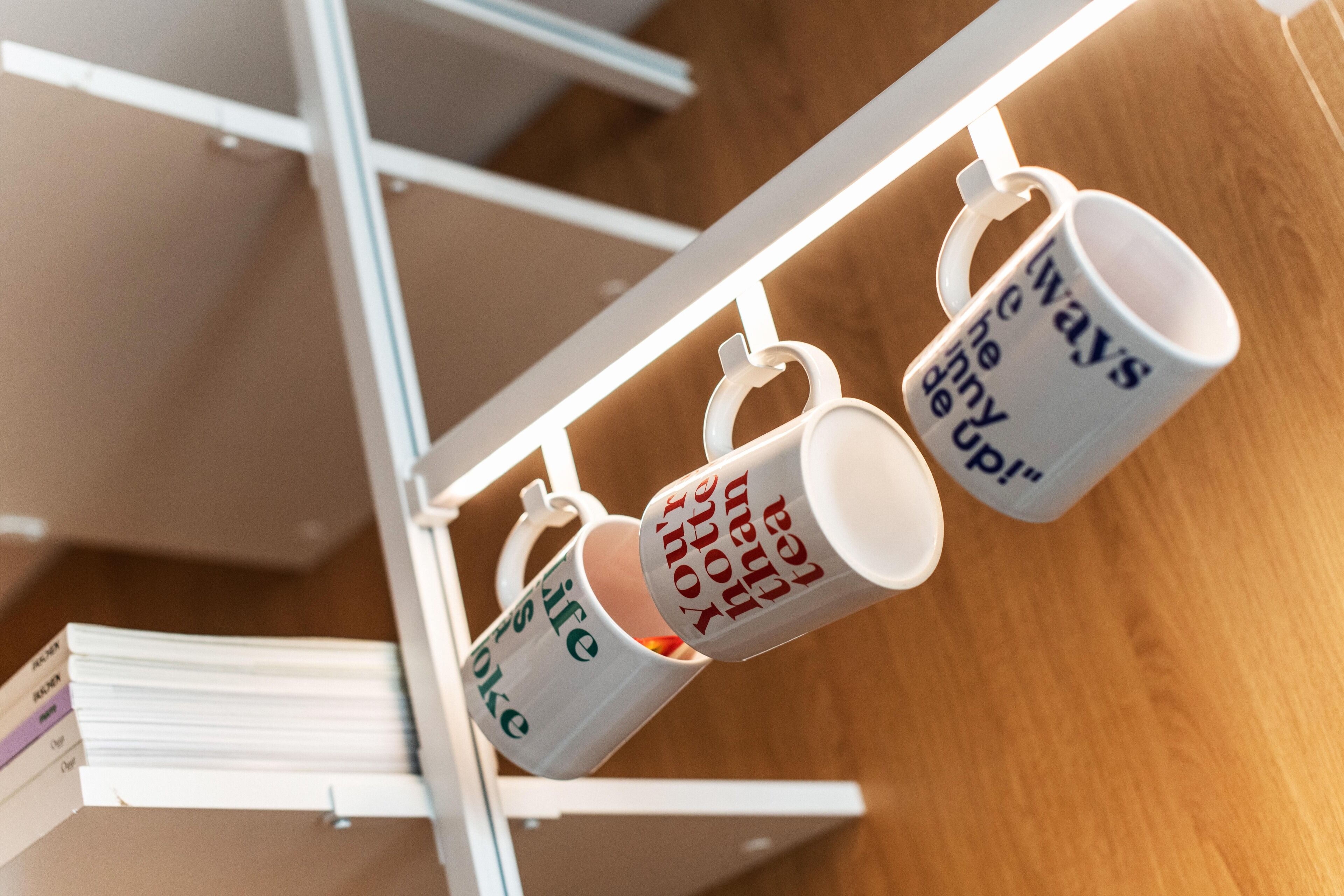 Tres tazas blancas con texto colgadas en un estante metálico blanco.