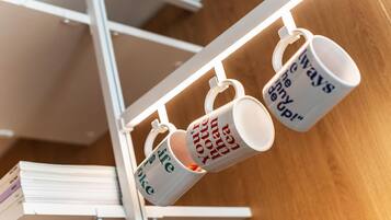 Tres tazas blancas con texto colgadas en un estante metálico blanco.