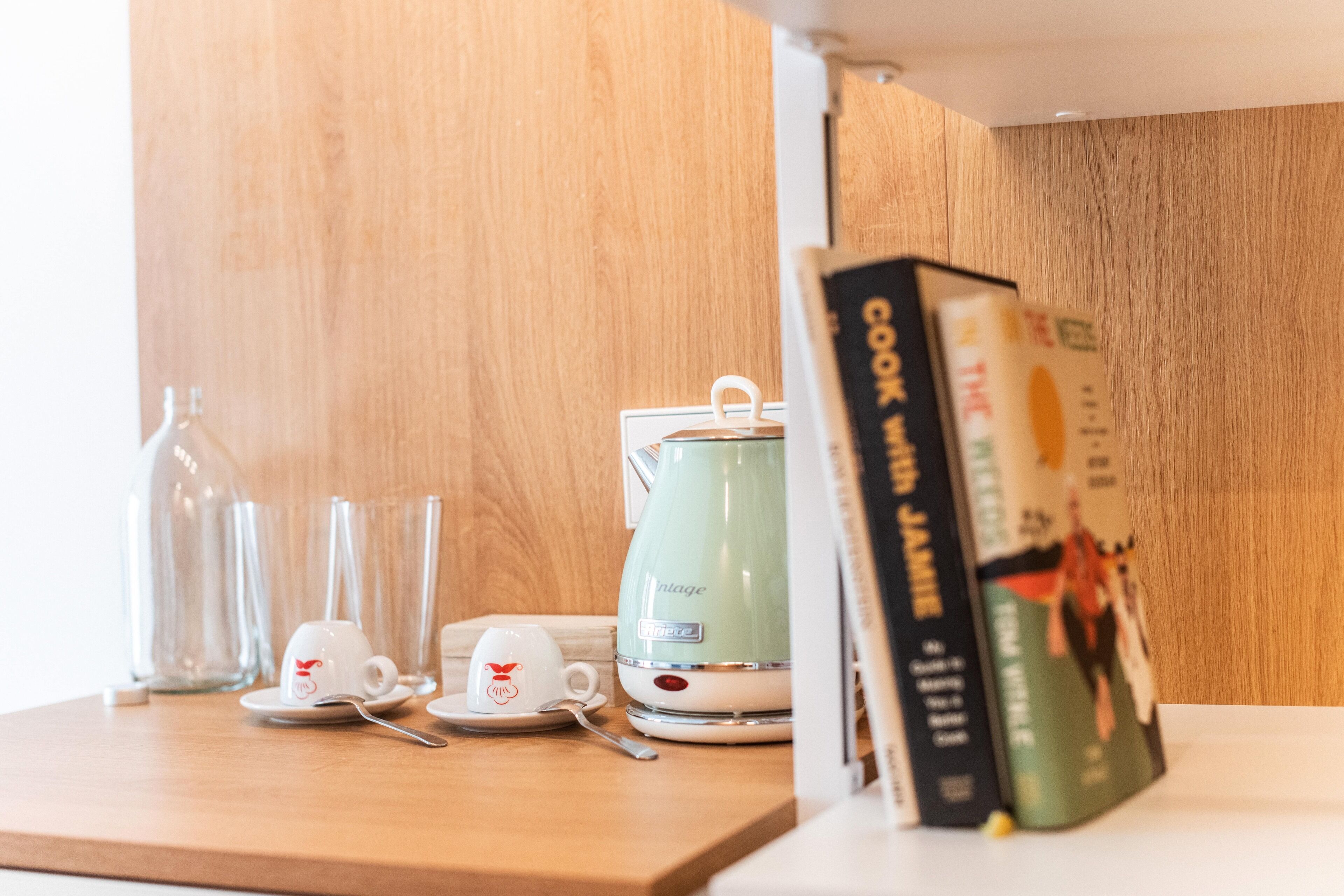 A kitchen counter with a green coffee maker, two white cups, and a glass bottle.
