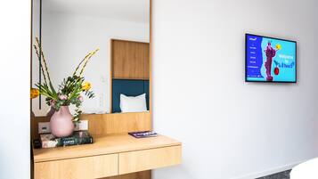 Un baño moderno con tocador de madera, un jarrón rosa con flores y un televisor mostrando un mensaje de bienvenida.