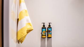 Un baño con una toalla amarilla y blanca a rayas colgada en un perchero, y dos botellas de champú y acondicionador en la pared.