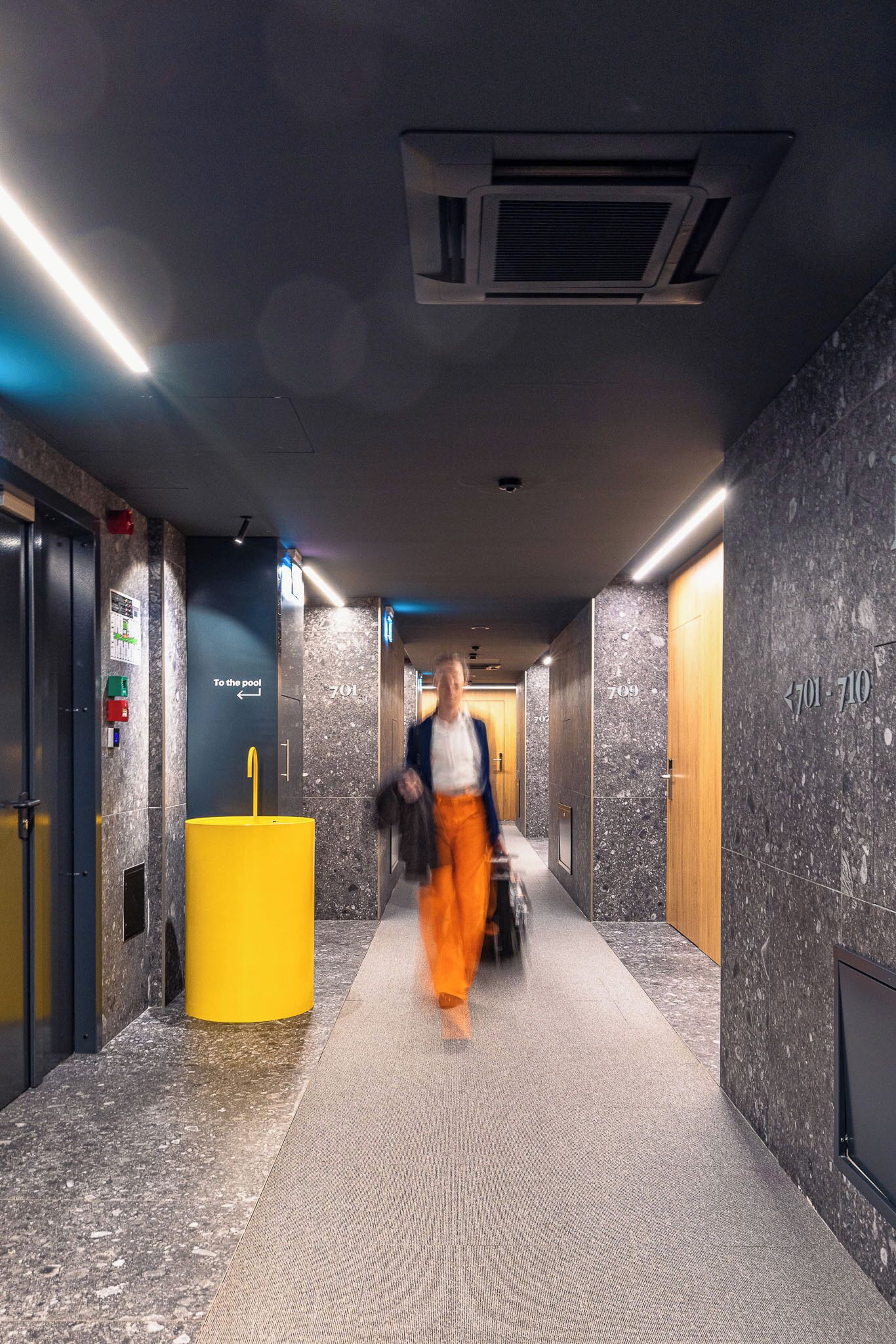 A hotel corridor with a marble wall, a yellow pillar, and a sign pointing to the pool.