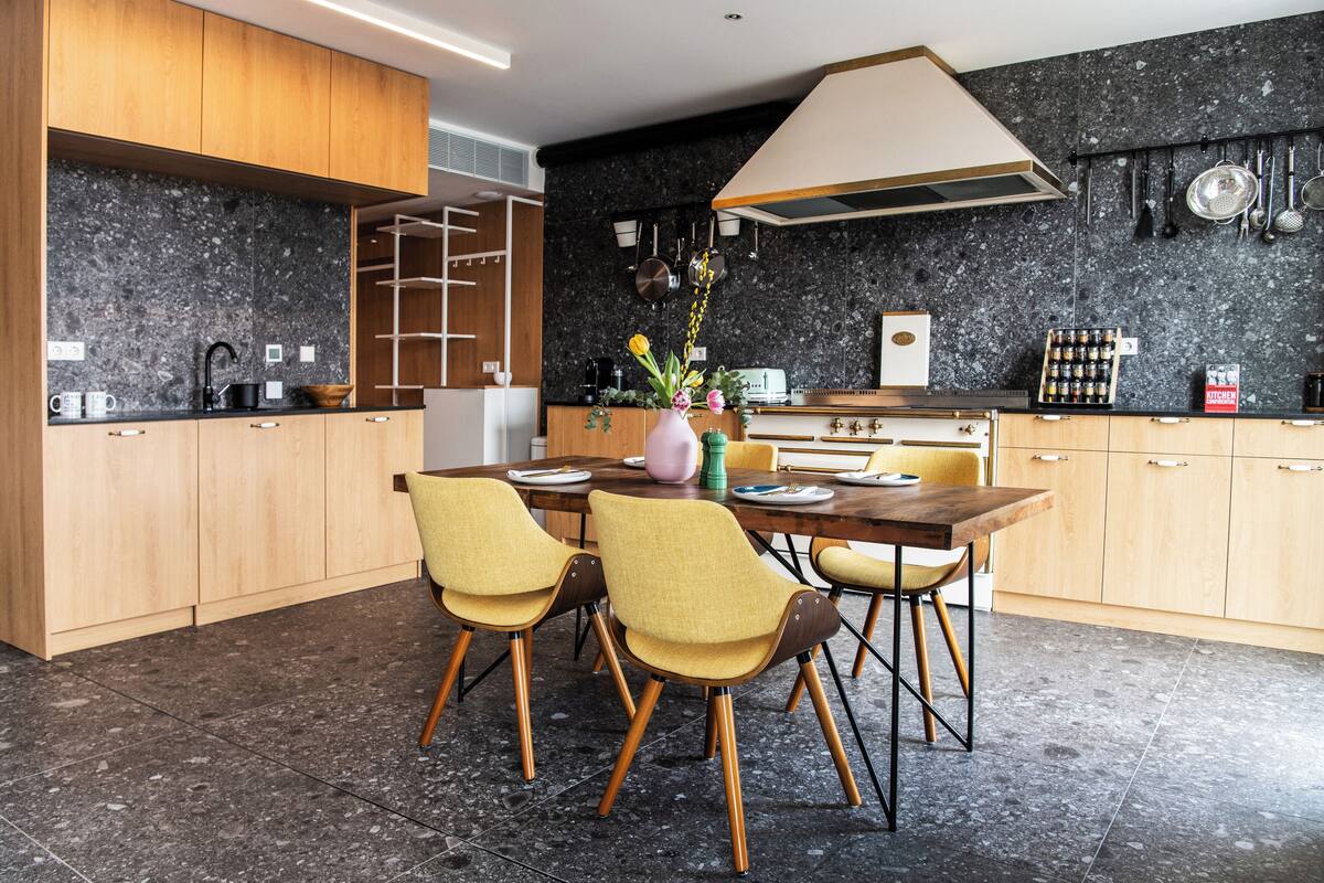 A modern kitchen with wooden cabinets, a granite countertop, and a dining area with yellow chairs.