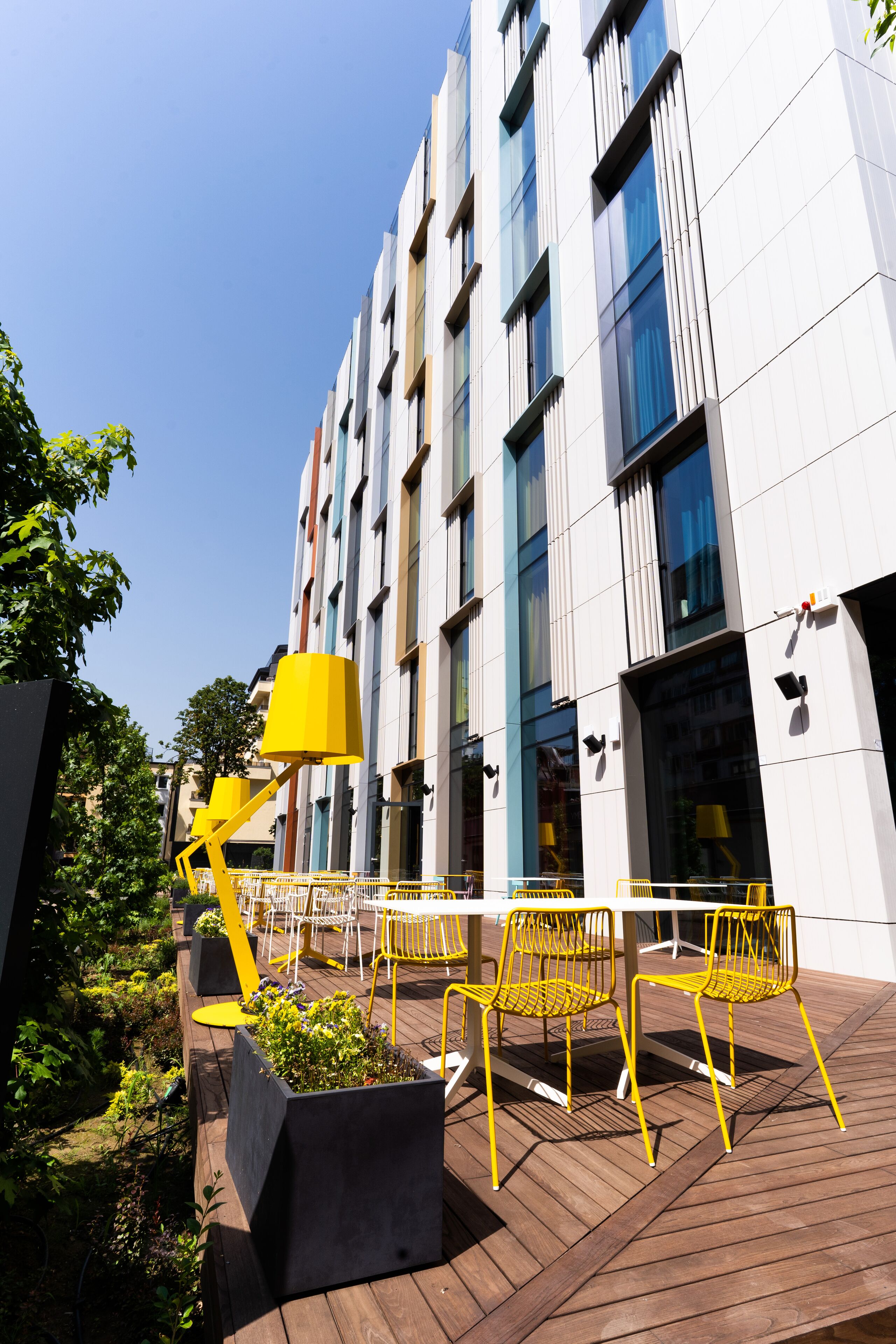Un bâtiment moderne doté d’une cour intérieure avec des chaises jaunes et un jardinier.