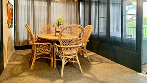 Un coin repas avec une table ronde et des chaises en osier, un ventilateur de plafond et de grandes fenêtres avec des rideaux.