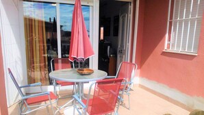 Une terrasse avec une table ronde et quatre chaises, un parasol rouge et une clôture en bois.