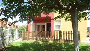 Une cour clôturée avec un arbre, un bâtiment à la façade rouge et jaune, et un ciel dégagé.