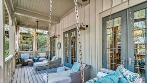 A covered porch with wicker furniture, a swing, and a view of the outdoors. - Pet Friendly Designer Gem with LSV and Bikes 100 Yards to Camp WaterColor (Santa Rosa Beach)