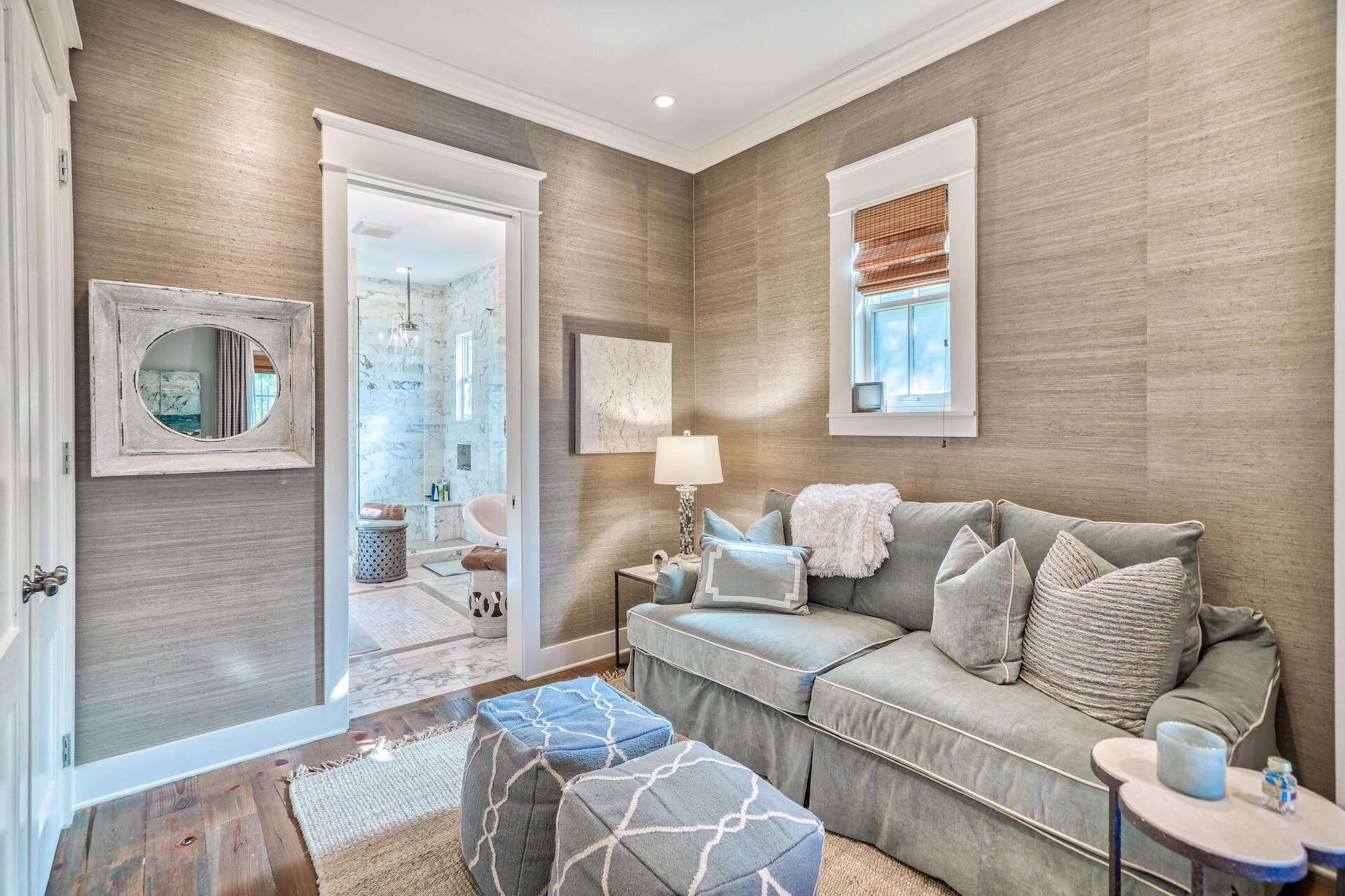 A modern living room with a grey sofa, patterned ottomans, a small side table, and a window with blinds.