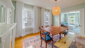 A dining area with a wooden table and chairs, a hanging light fixture, and a view of the outdoors through large windows. - Fun in the Sun Home with Game Shed, Near Beach (Cape Charles)