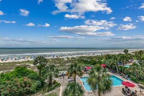 Relax by the pool surrounded by lush greenery and palm trees, with access to the beach and ocean views.