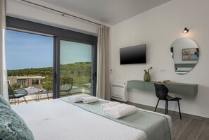 A hotel room with a bed, a desk, a chair, a TV, and a large window offering a view of the outdoors.