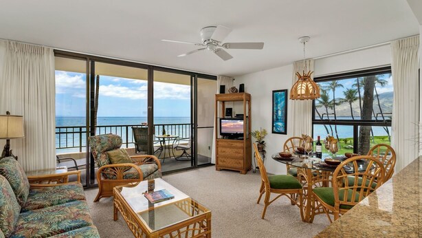 Ein geräumiges Wohnzimmer mit einem großen Schiebeglasfenster zum Balkon, einem Deckenventilator, einem Essbereich mit Tisch und Stühlen sowie einem Fernseher auf einer Holzeinrichtung.