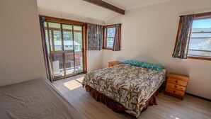 A bedroom with a large bed, a wooden nightstand, a dresser, and a sliding glass door leading to an outdoor area. - Beachside, Pet friendly, Paradise. (Black Head)