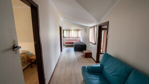 A narrow hallway with a teal sofa, a bed with a red blanket, and a small table with a colorful blanket. - Beachside, Pet friendly, Paradise. (Black Head)
