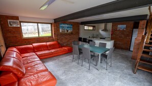 A kitchen with a dining area, a red leather sofa, and a brick wall. - Beachside, Pet friendly, Paradise. (Black Head)
