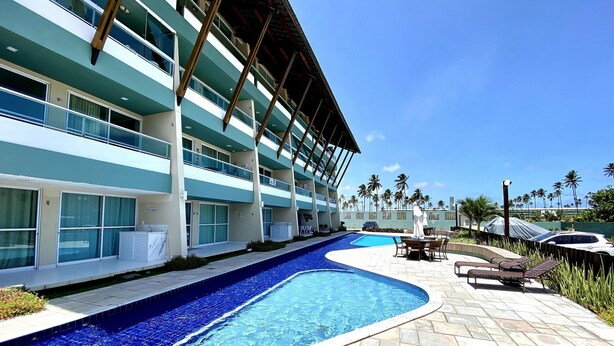 A hotel with a swimming pool, outdoor seating, and a view of palm trees. - Villas do Atlântico próximo ao mar (Ipojuca)