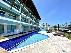 A hotel with a swimming pool, outdoor seating, and a view of palm trees.