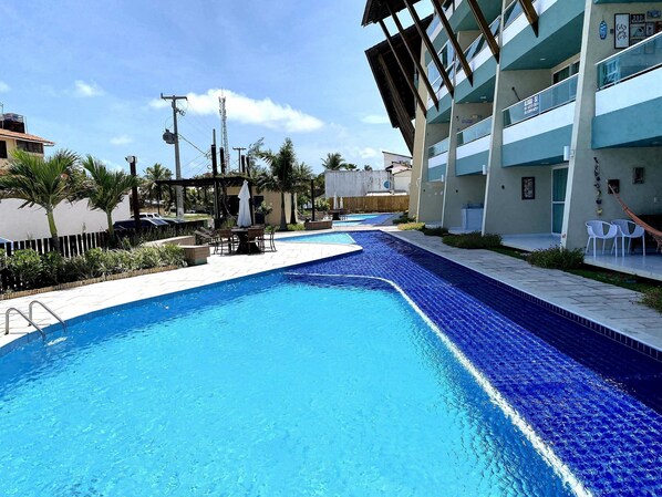 A swimming pool with a tiled edge, surrounded by a patio area with chairs and a table.