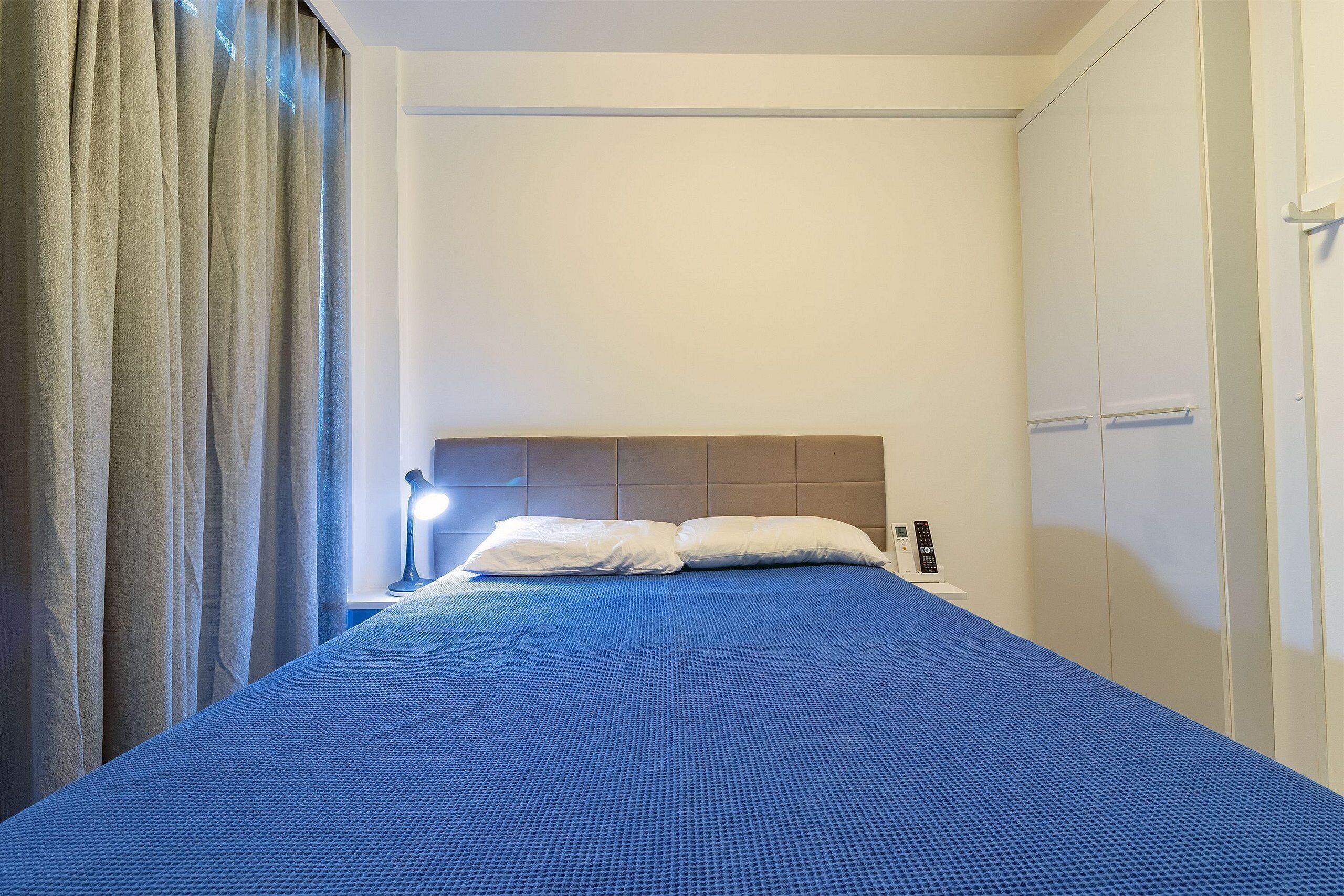 Ein Hotelzimmer mit Bett, Vorhängen, einer Nachttischlampe und einem Schrank.