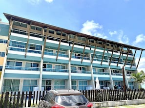 A multi-story hotel with balconies, a car parked in front, and a clear blue sky.