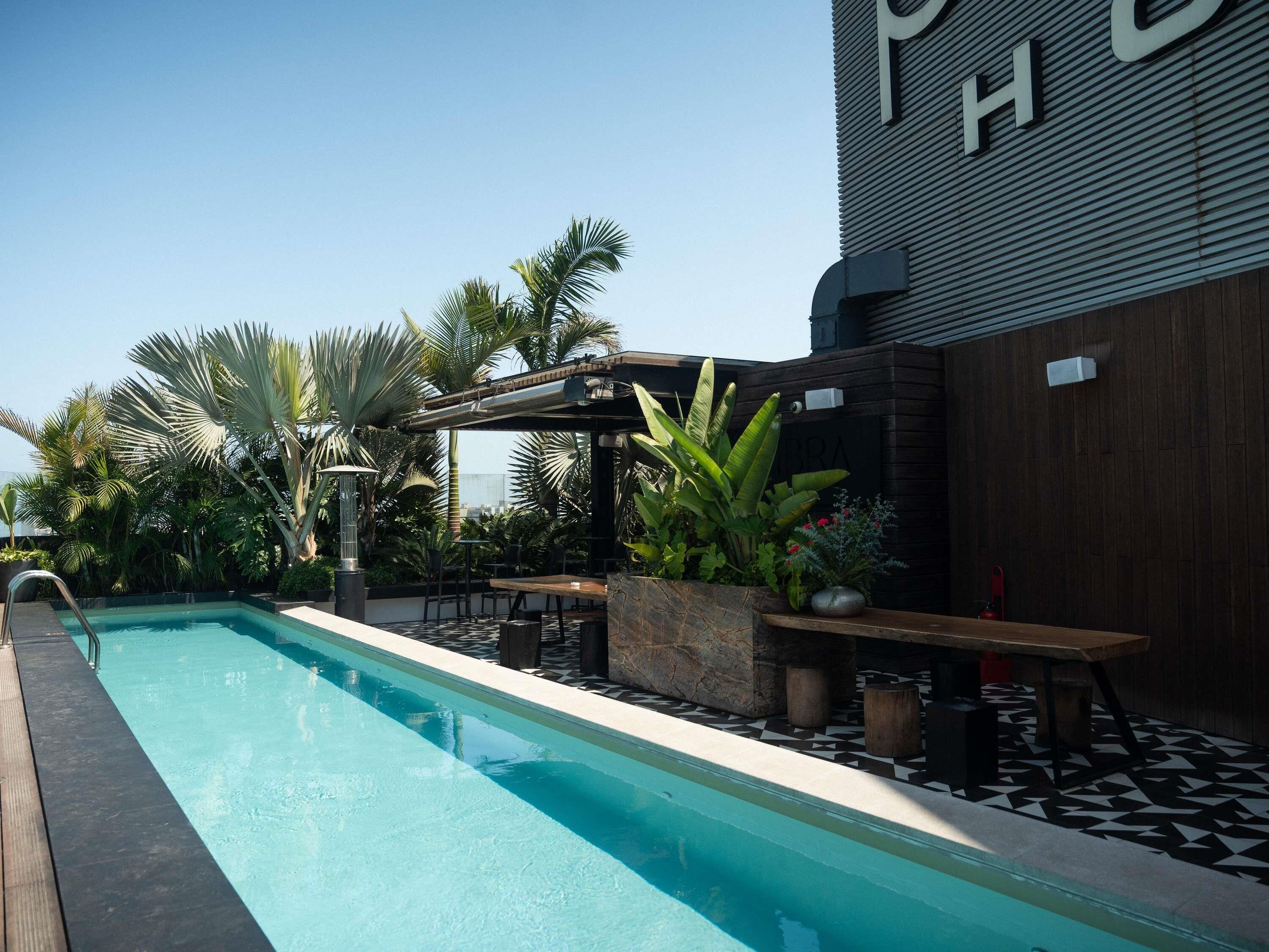 A pool area with a wooden deck, outdoor seating, and tropical plants.