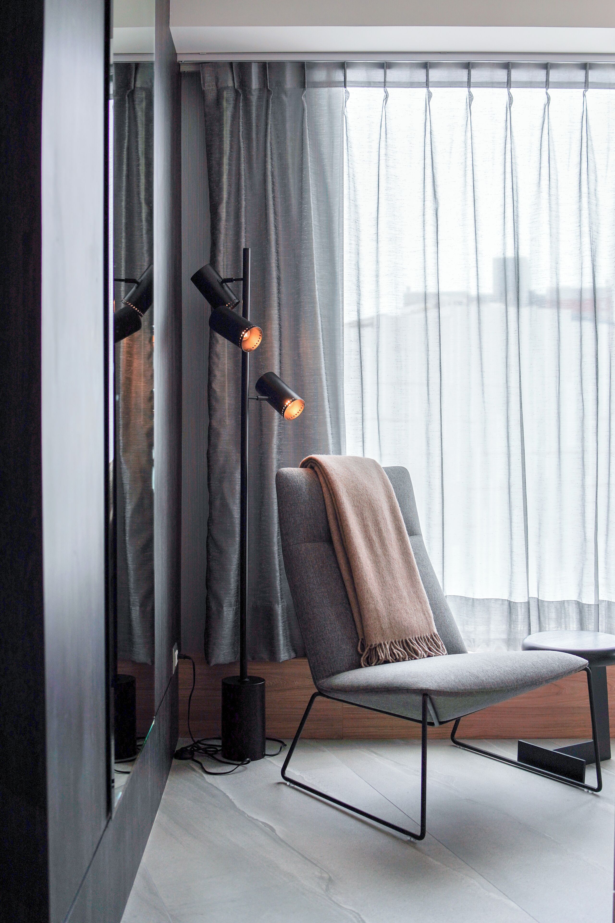 A modern living room with a grey armchair, a floor lamp, and a large window with grey curtains.