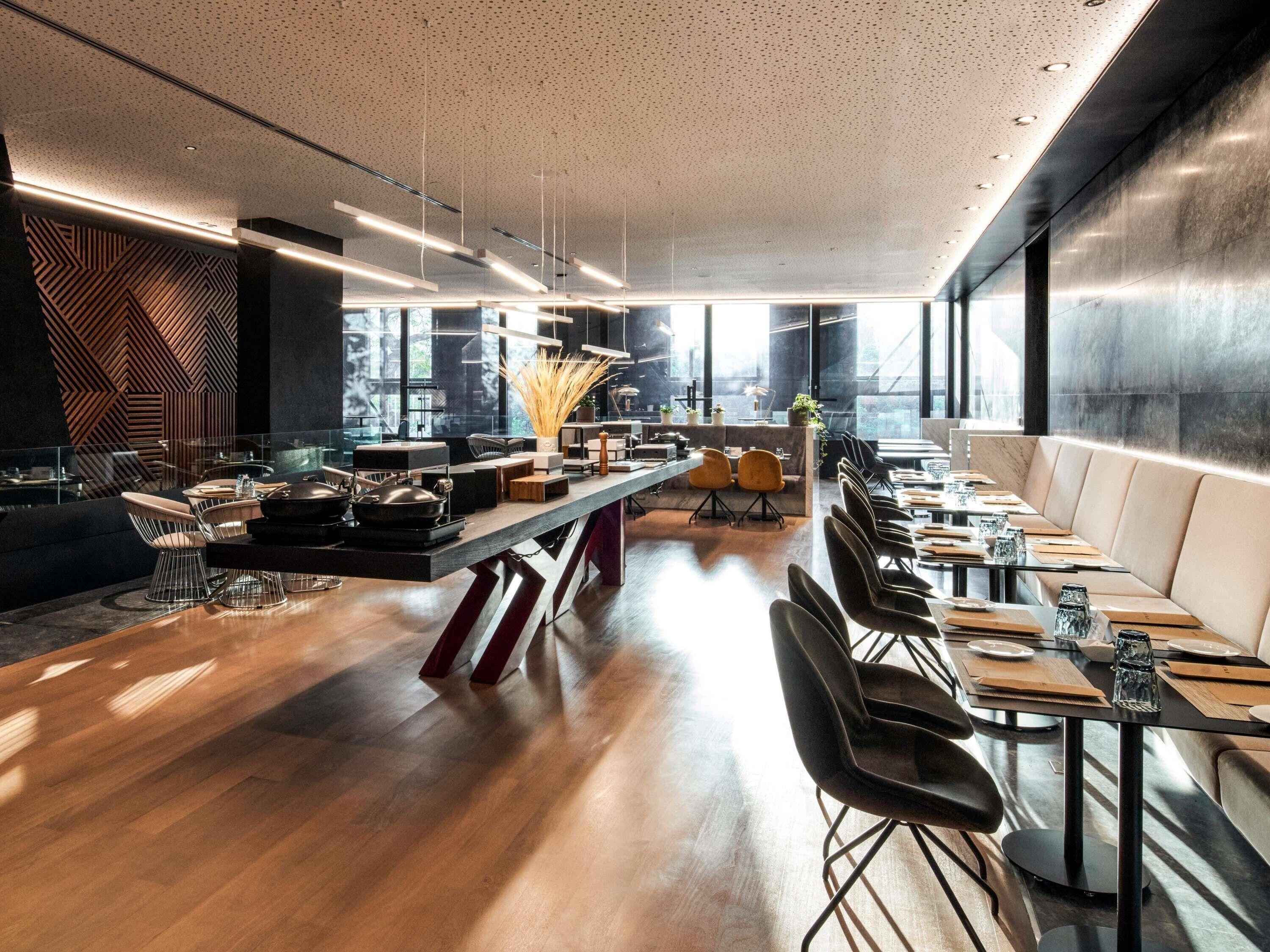 A modern dining area with a long table, chairs, and a bar area with stools.