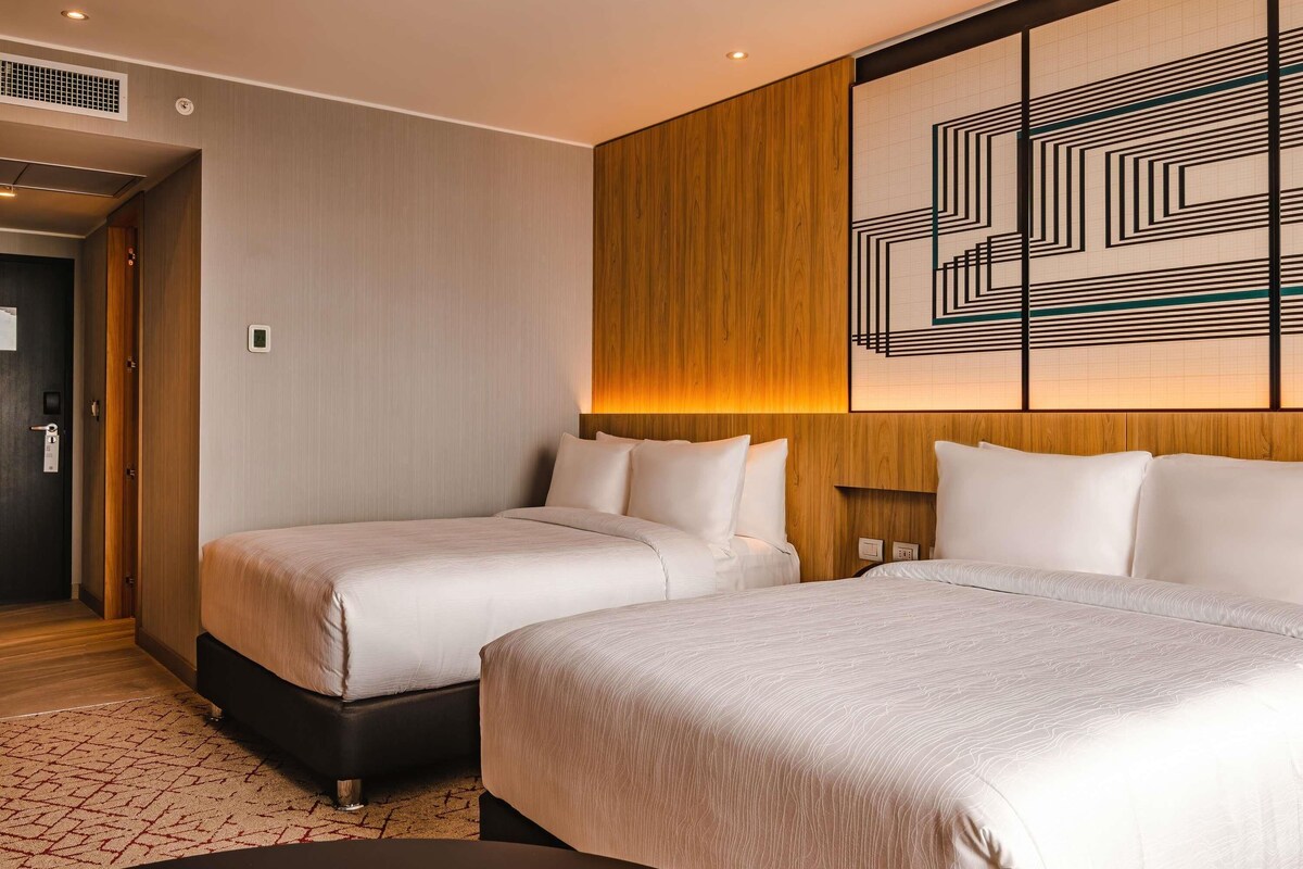 A hotel room with two beds, a wooden accent wall, and a geometric wall art piece.