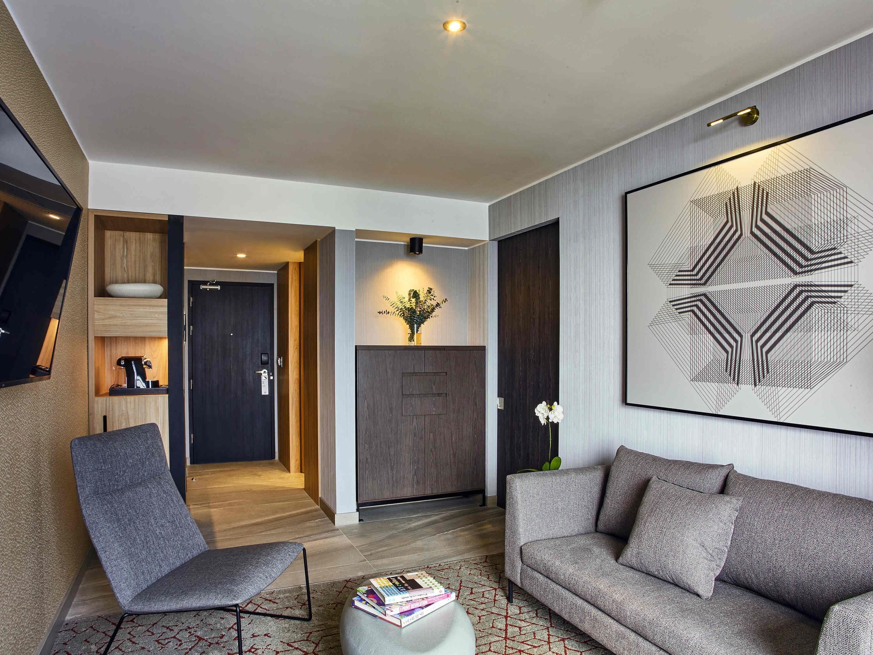 A modern living room with a sofa, a chair, a coffee machine, and a door leading to another room.