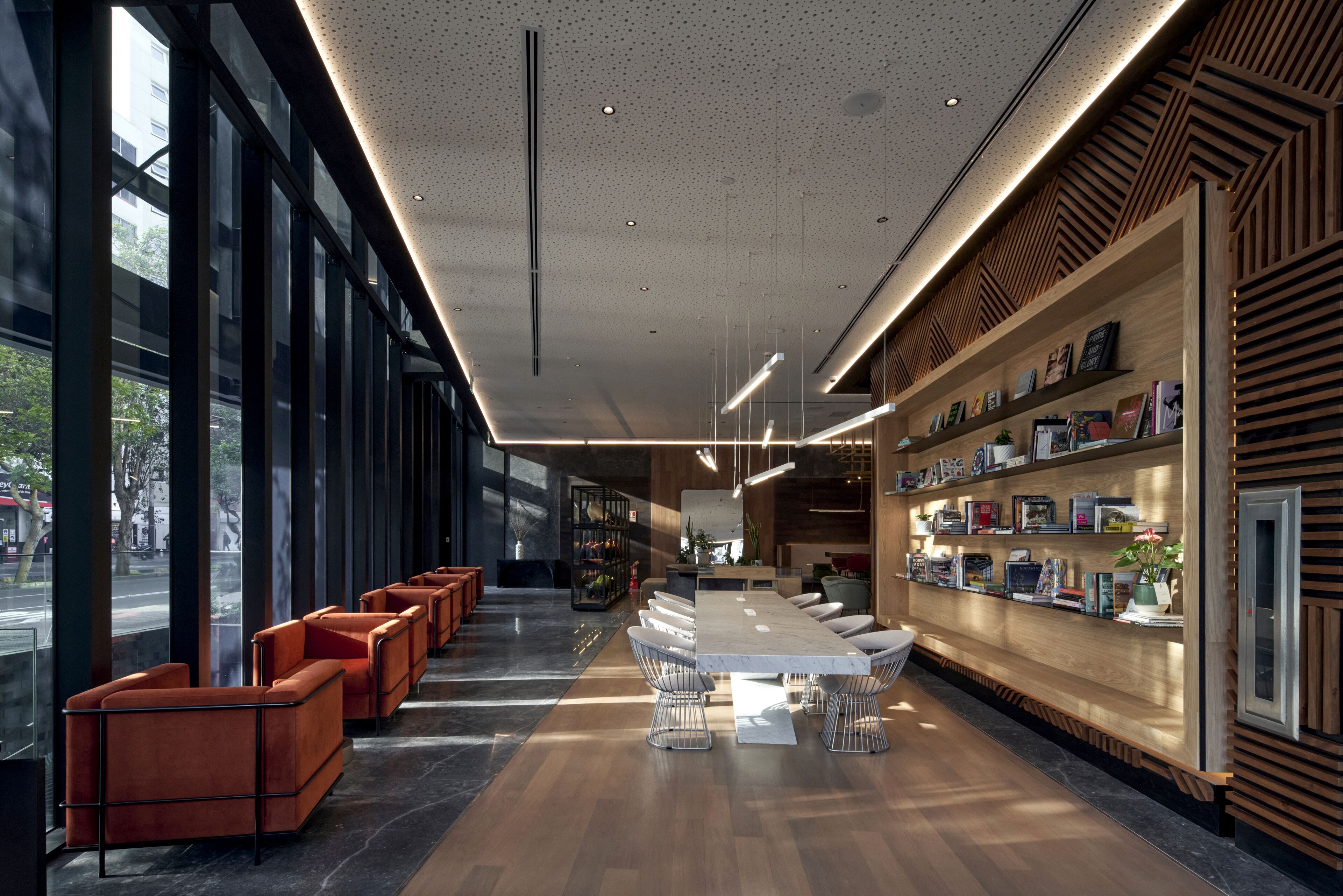 Un intérieur moderne avec une longue table à manger, des chaises orange et une bibliothèque remplie de livres et d’objets décoratifs.