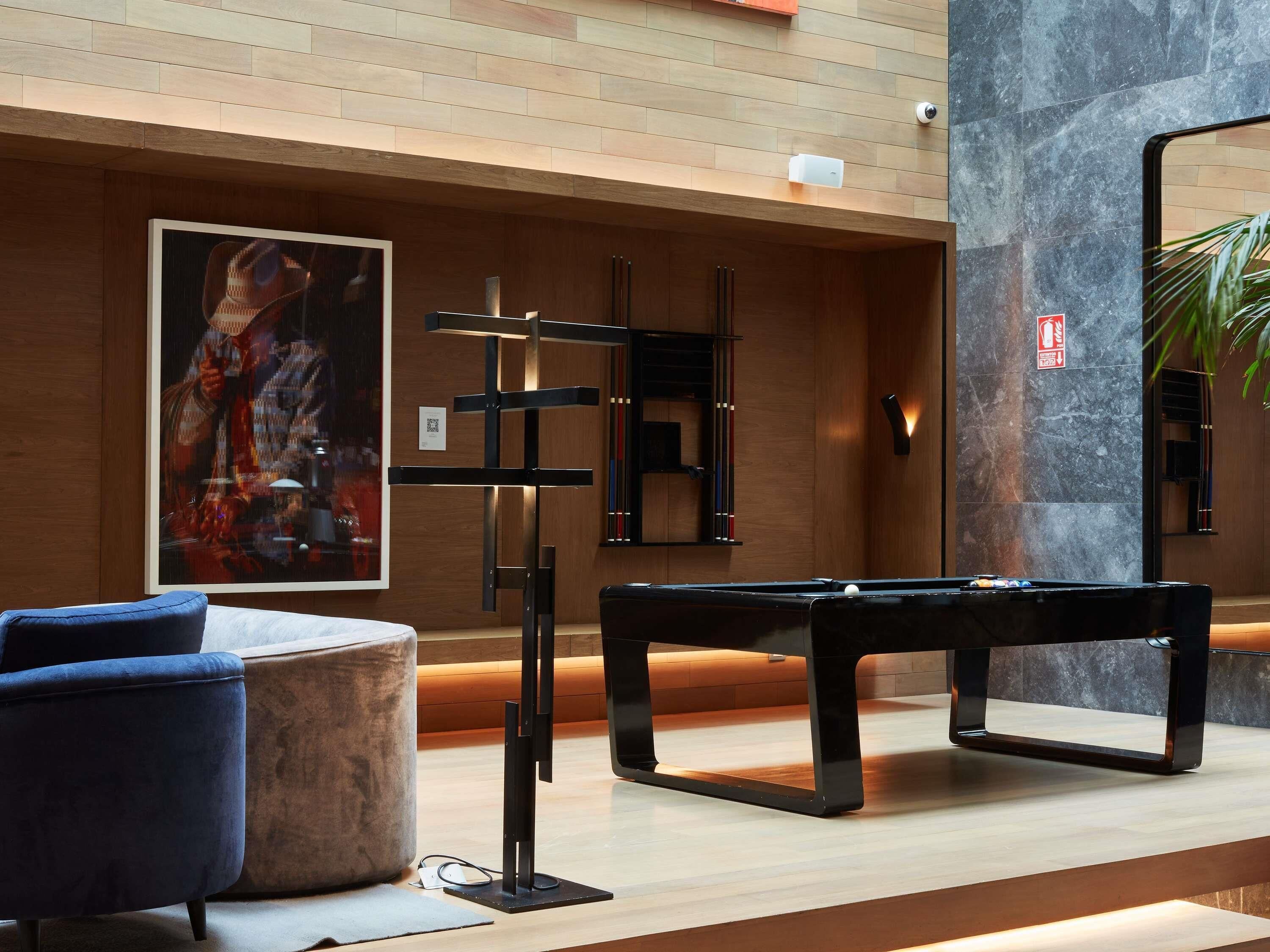 Una mesa de billar en una habitación moderna con piso de madera, una silla azul y una obra enmarcada en la pared.