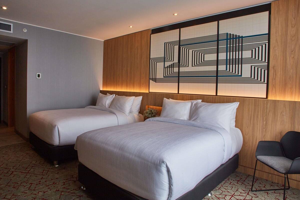 A hotel room with two beds, a modern wall art piece, and a wooden accent wall.