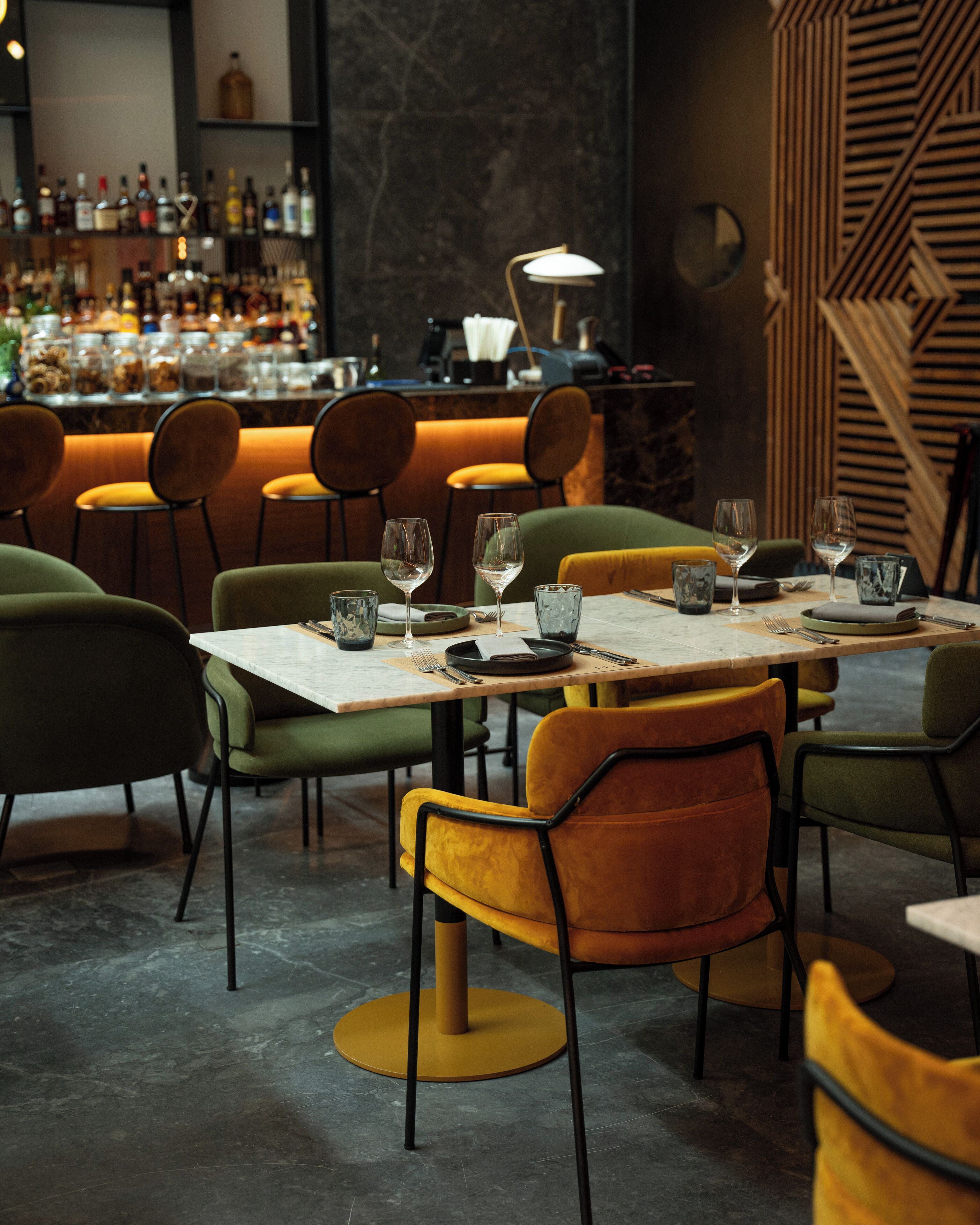 A restaurant interior with round tables, chairs, and a bar area in the background.