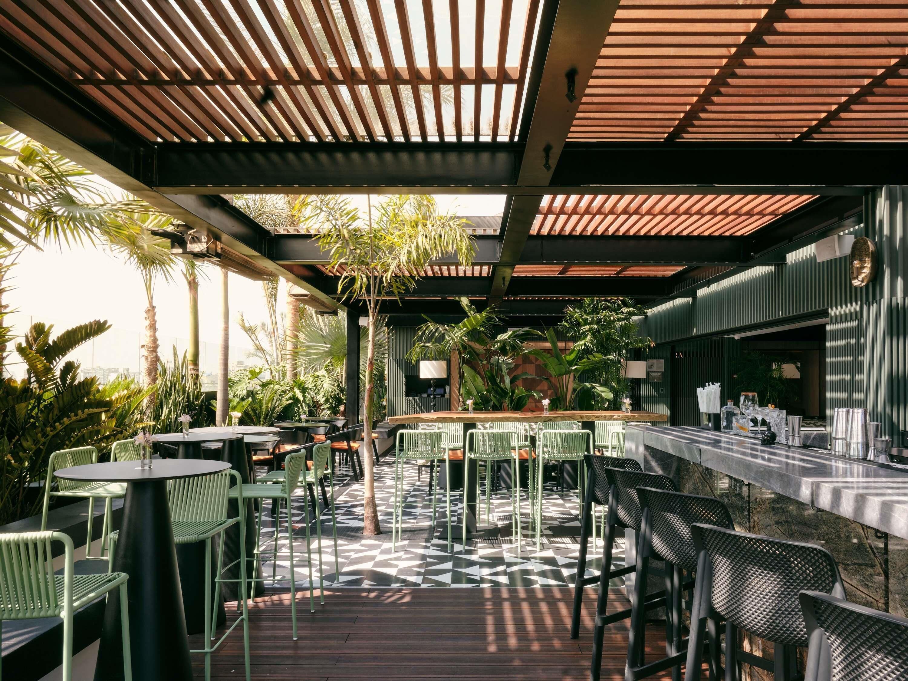 An outdoor patio with tables and chairs, a bar area, and lush greenery.