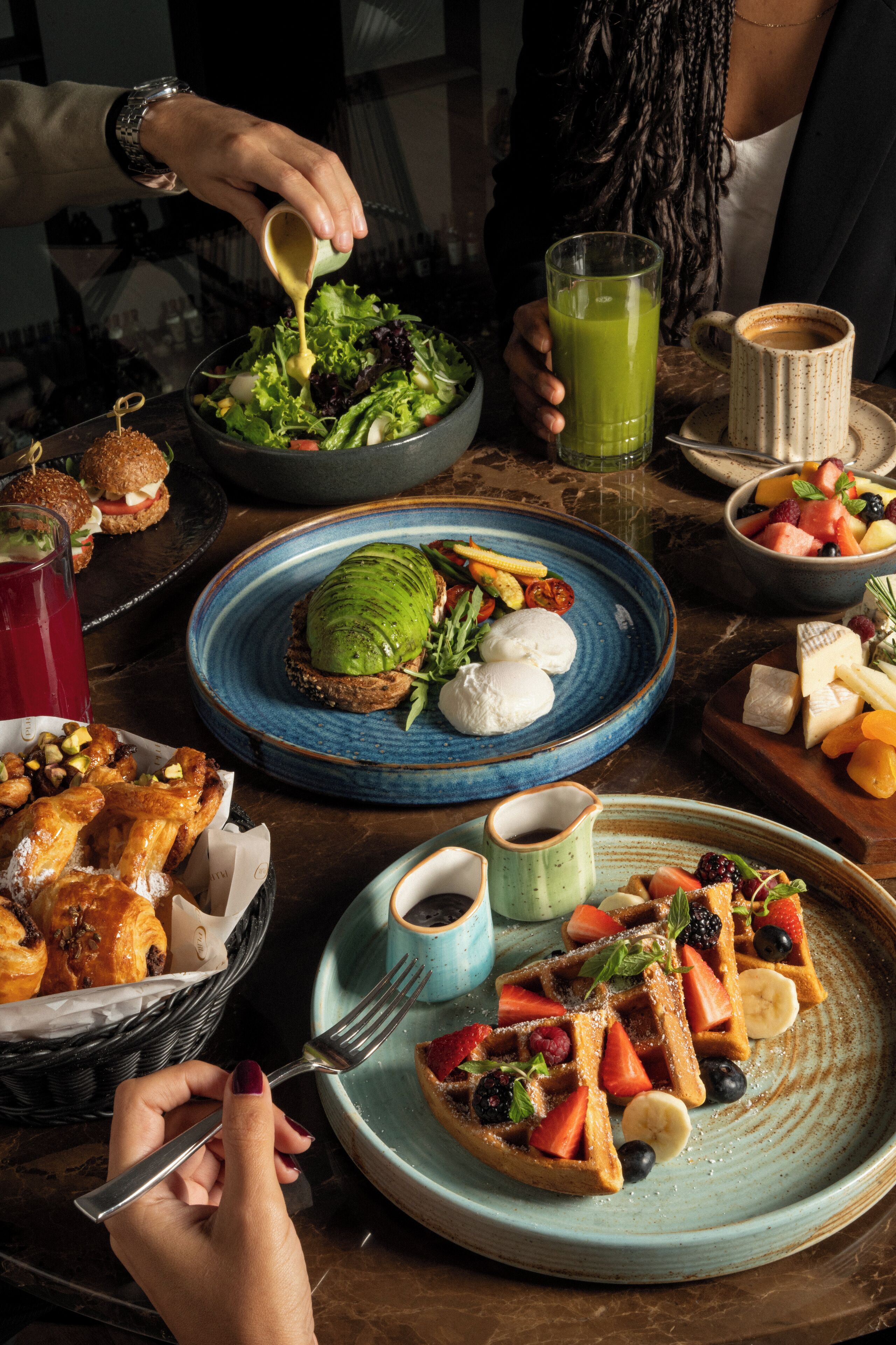 A dining table with various dishes including a salad, fruit, waffles, and a sandwich.
