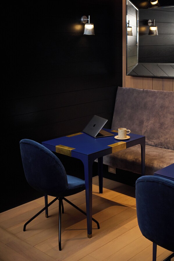 A modern room with a dark wooden wall, a blue table with a laptop, a white mug, and two blue chairs.