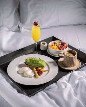 A breakfast tray with a plate of food, a glass of orange juice, a bowl of fruit, and a cup of coffee on a bed.