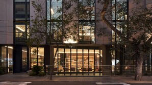 A modern building with large glass windows, a visible interior with seating, and a tree in front. - Pullman Lima Miraflores (Lima)