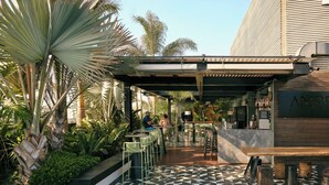 An outdoor bar area with a pool, surrounded by tropical plants and palm trees. - Pullman Lima Miraflores (Lima)