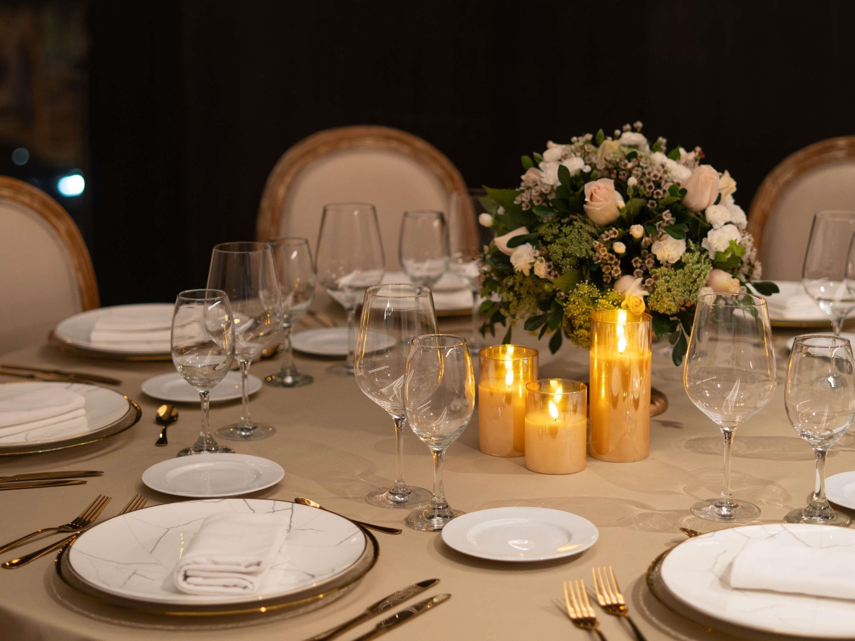 Una mesa dispuesta para una cena formal, con platos blancos, copas de cristal transparentes y cubiertos dorados.