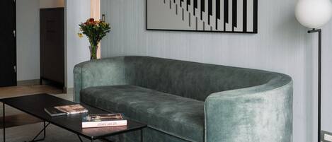 A modern living room with a grey sofa, a black coffee table with books, a black rug, and a large abstract art piece on the wall.