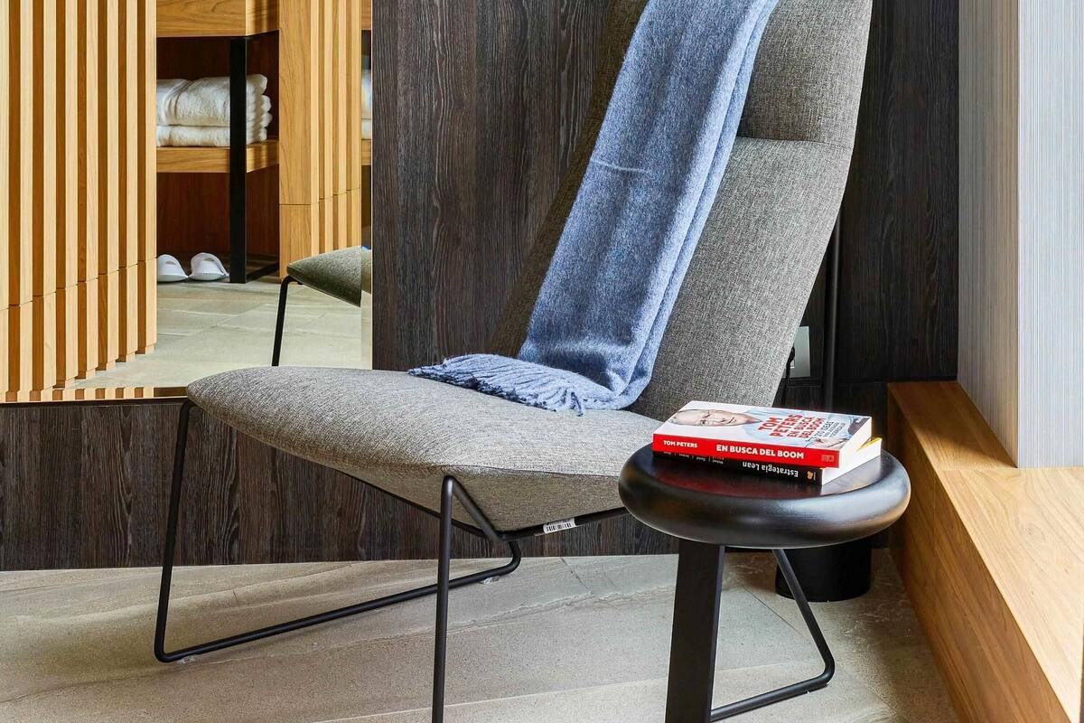 A modern chair with a towel draped over it, a book on the armrest, and a wooden shelf in the background.