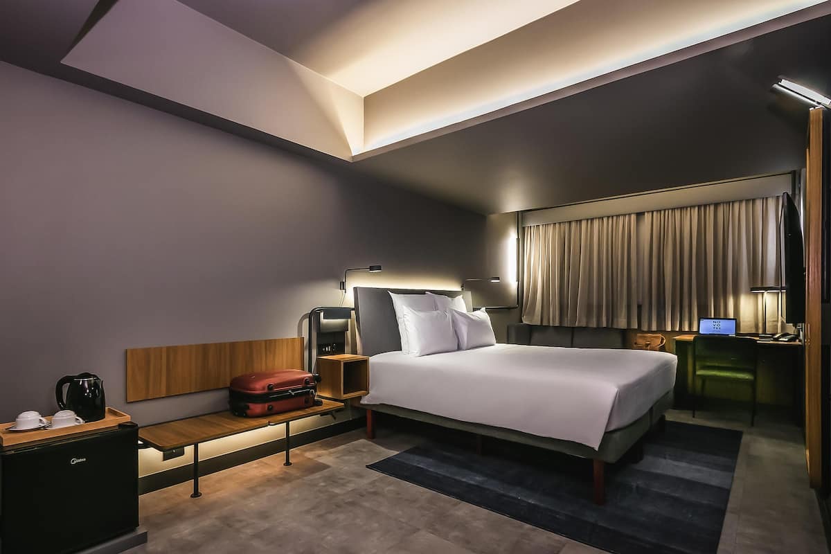 Ein modernes Hotelzimmer mit einem großen Bett, Nachttischen, einem Schreibtisch mit Computer und Blick auf die Stadt.