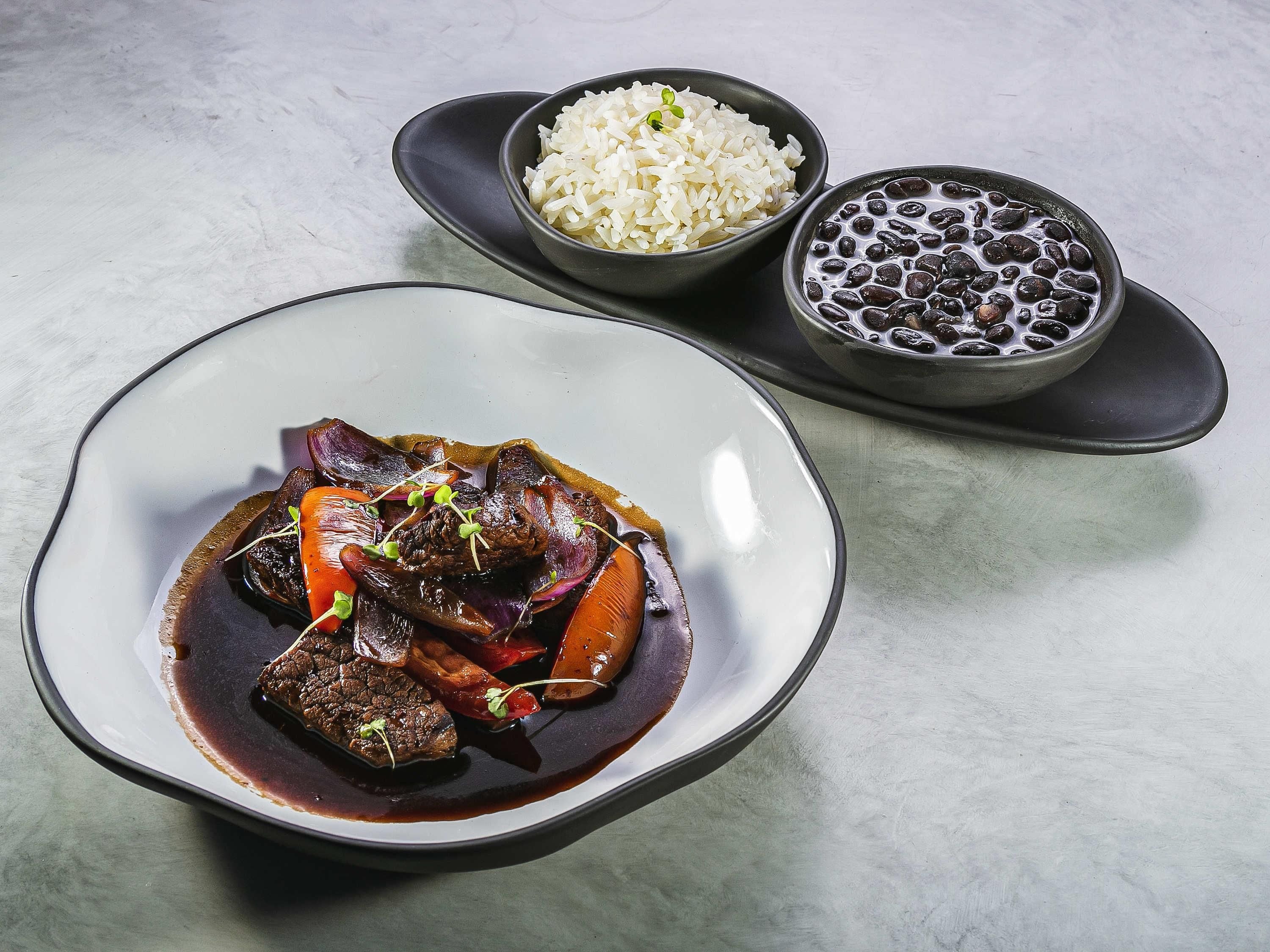 A plate of beef with vegetables and a bowl of rice.