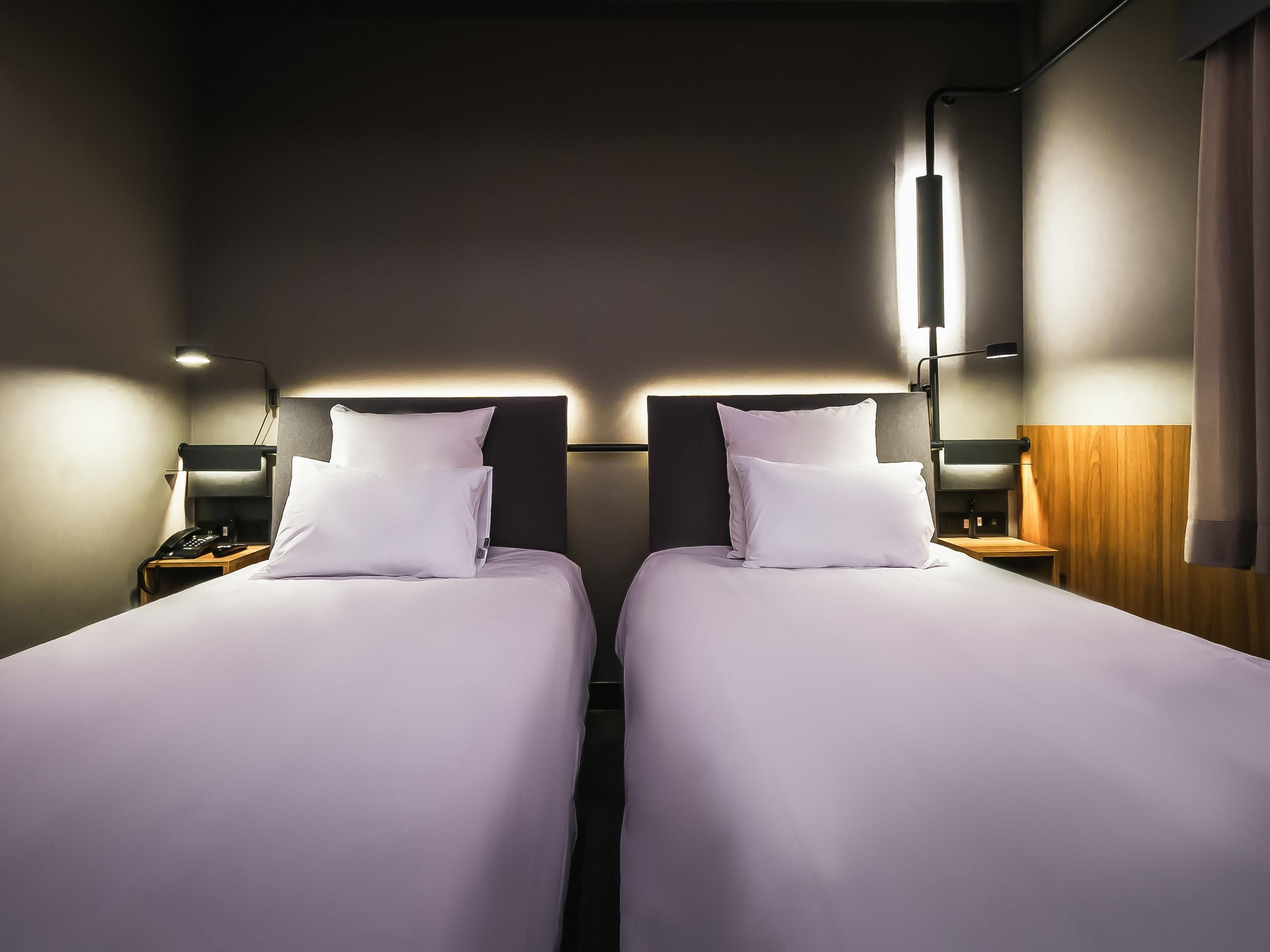 A hotel room with two beds, bedside tables, lamps, and a wooden accent wall.